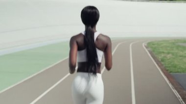 Spor elbiseli güzel Afrikalı bir kadının arkadan görünüşü raylarda koşuyor.