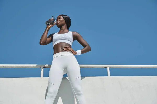 Низкий угол обзора красивой молодой африканской женщины в спортивной одежде питьевой воды — стоковое фото