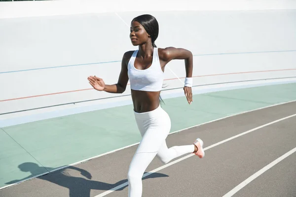 Belle jeune femme africaine en vêtements de sport courir sur la piste en plein air — Photo