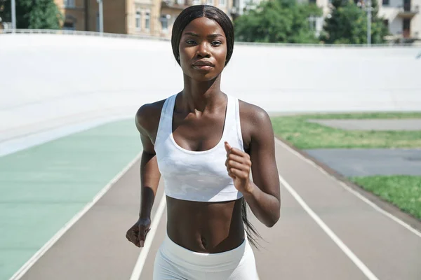 Beautiful young African woman in sports clothing running on track outdoors — Stock Photo, Image