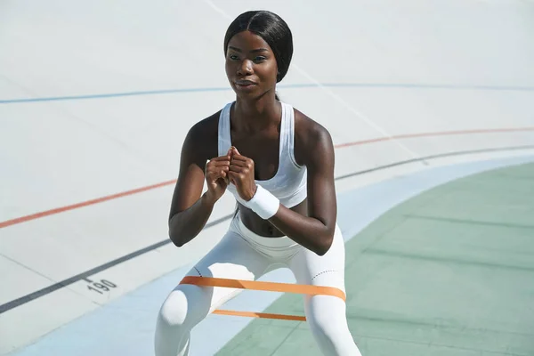 Koncentreret ung afrikansk kvinde i sportstøj udøver udendørs - Stock-foto