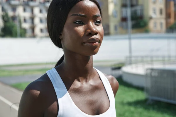 Close-up of beautiful young African woman in sports clothing running on track outdoors — Stock Photo, Image