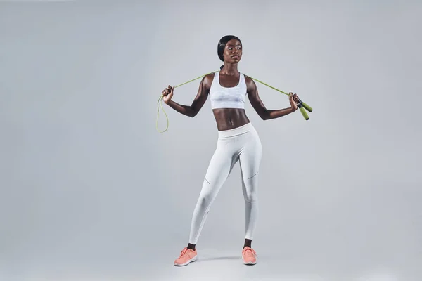 Mujer africana joven y confiada en ropa deportiva que lleva una cuerda de salto en los hombros —  Fotos de Stock