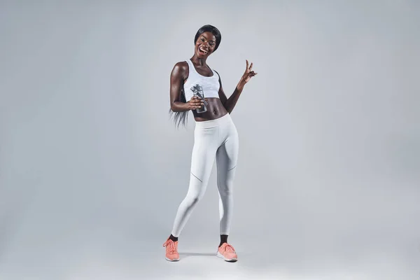 Gelukkig jong Afrikaans vrouw in sport kleding vasthouden fles met water en gebaren — Stockfoto