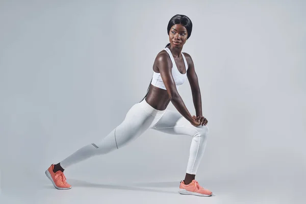 Hermosa mujer africana joven en ropa deportiva que se extiende sobre fondo gris —  Fotos de Stock