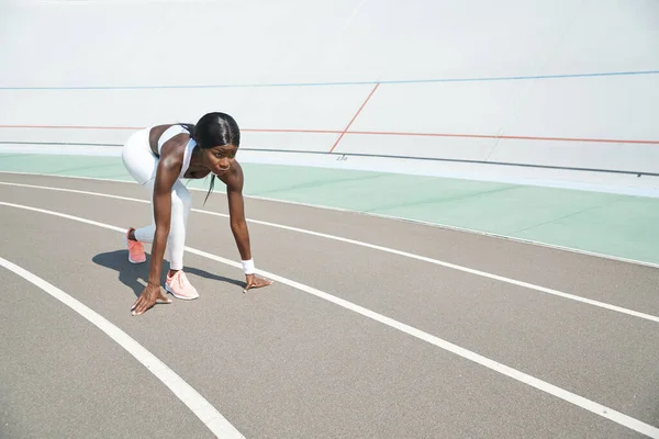 Schöne junge Afrikanerin steht in Startposition auf Laufbahn im Freien — Stockfoto