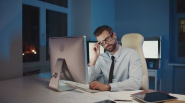 Ofiste geç saatlere kadar kalırken kameraya bakıp gülümseyen genç adam. 