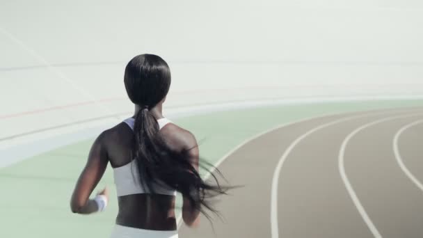Rear view of young African woman in sports clothing running on track outdoors — Stock Video