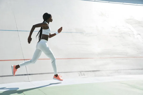 Beautiful young African woman in sports clothing running on track outdoors — Stock Photo, Image