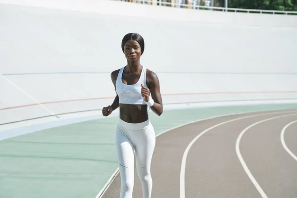 Fiduciosa giovane donna africana in abbigliamento sportivo in esecuzione in pista all'aperto — Foto Stock