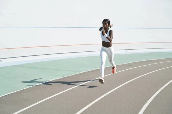 Krásná mladá africká žena ve sportovním oblečení běží na trati venku — Stock fotografie