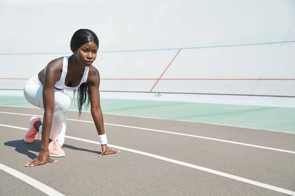 Schöne junge Afrikanerin steht in Startposition auf Laufbahn im Freien — Stockfoto