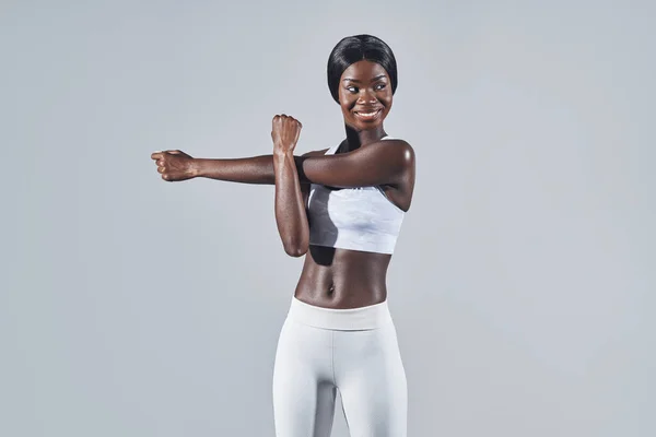 Hermosa mujer africana joven en ropa deportiva que se extiende sobre fondo gris —  Fotos de Stock