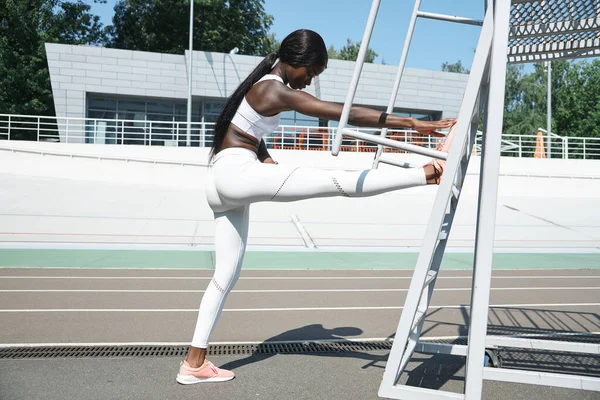 Mujer africana joven y segura en ropa deportiva haciendo ejercicios de estiramiento al aire libre — Foto de Stock