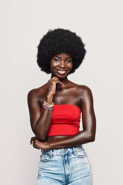 Schöne junge Afrikanerin blickt in die Kamera und lächelt vor grauem Hintergrund — Stockfoto