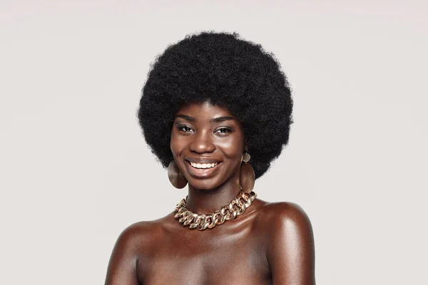 Arckép gyönyörű fiatal afrikai nő arany ékszerek néz kamera és mosolygós — Stock Fotó