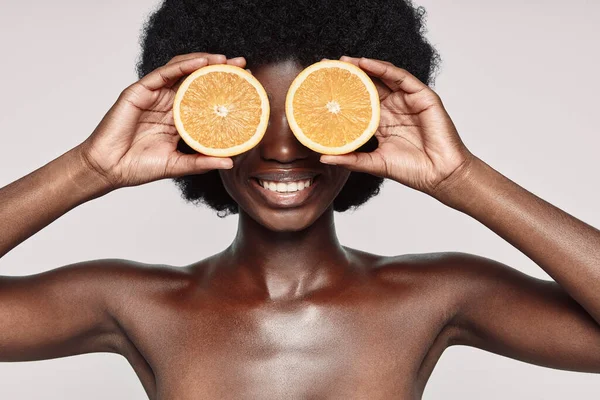 Портрет красивой молодой африканской женщины, закрывающей глаза оранжевыми осколками и улыбающейся — стоковое фото