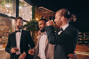 Takım elbiseli, elinde viski bardaklarıyla eğlenen üç mutlu adam.