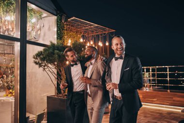 Takım elbiseli, elinde viski bardaklarıyla eğlenen üç mutlu adam.