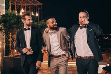 Takım elbiseli üç yakışıklı adam viski içip eğlenirken iletişim kuruyor.