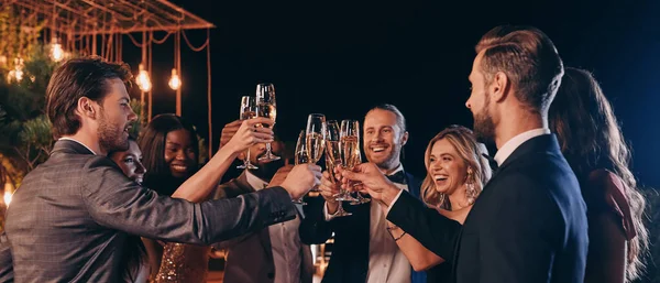Grupa pięknych ludzi w formalnych strojach wznoszących toast szampanem i uśmiechających się spędzając czas na luksusowej imprezie — Zdjęcie stockowe