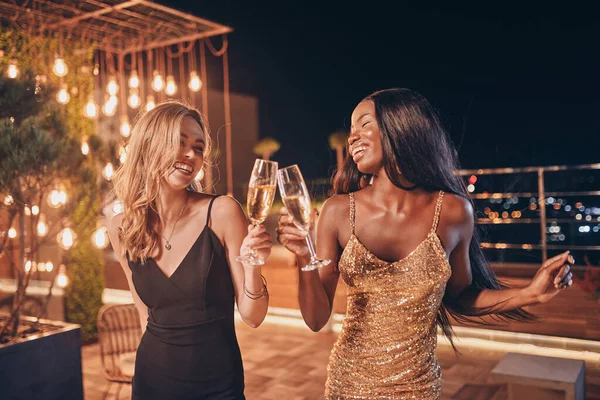 Duas mulheres bonitas em vestidos de noite dançando e sorrindo enquanto passa o tempo em festa de luxo — Fotografia de Stock