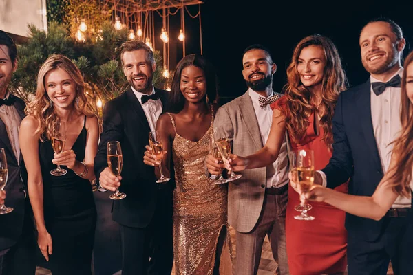 Grupo de personas en ropa formal brindando con champán y sonriendo mientras pasan tiempo en una fiesta de lujo — Foto de Stock