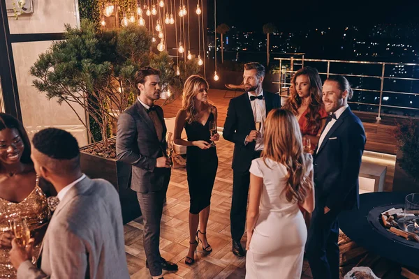 Grupo de personas en ropa formal comunicándose y sonriendo mientras pasan tiempo en una fiesta de lujo — Foto de Stock