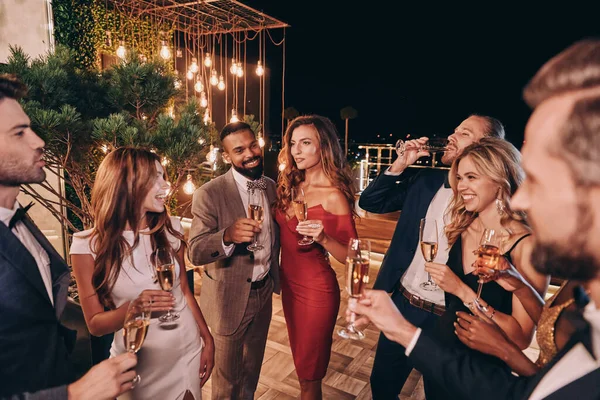 Grupo de jóvenes guapos en ropa formal comunicándose y sonriendo mientras pasan tiempo en una fiesta de lujo — Foto de Stock