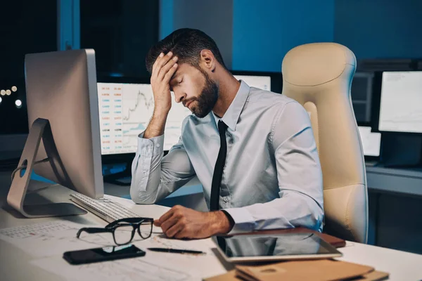 Frustrierter junger Mann in Hemd und Krawatte hat Kopfschmerzen, während er spät im Büro bleibt — Stockfoto