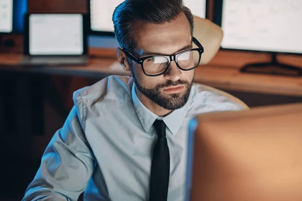 Sérieux jeune homme travaillant sur ordinateur tout en restant tard dans le bureau — Photo
