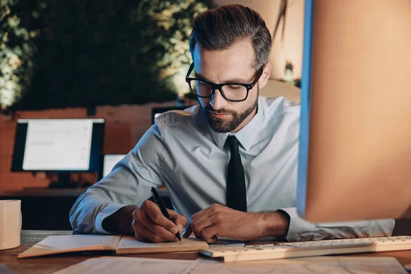 Confident young man making notes while staying late in the office — Stock Photo, Image