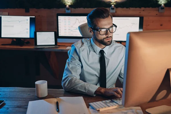 Konzentrierter junger Mann arbeitet am Computer, während er spät im Büro bleibt — Stockfoto