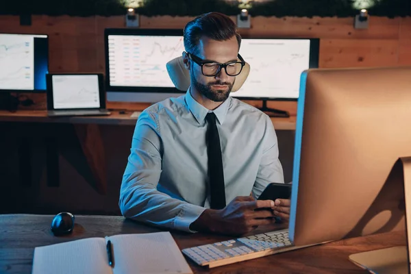 Selbstbewusster junger Mann arbeitet am Computer und bleibt spät im Büro — Stockfoto