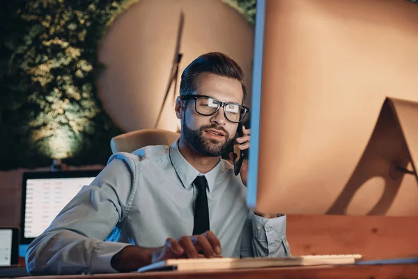 Ofiste geç saatlere kadar kalırken bilgisayarla çalışan ve cep telefonuyla konuşan kendine güvenen genç adam.