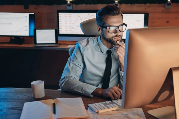 Konzentrierter junger Mann arbeitet am Computer, während er spät im Büro bleibt — Stockfoto
