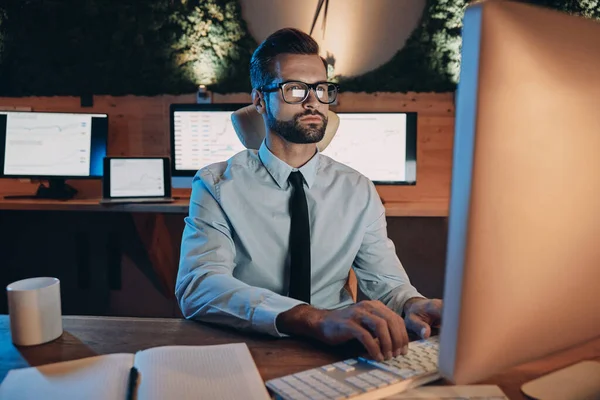 Уверенный молодой человек, работающий за компьютером, оставаясь допоздна в офисе — стоковое фото