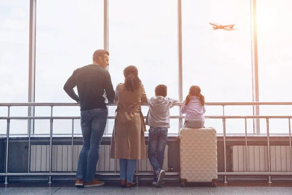 Toute la famille avec deux petits enfants regardant l'avion volant alors qu'ils se tenaient dans le terminal de l'aéroport — Photo