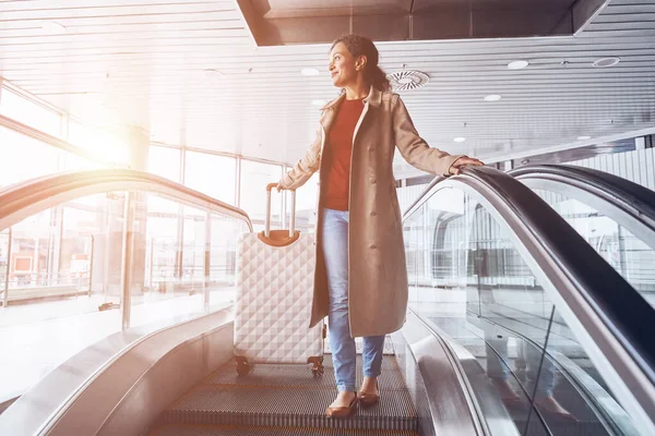 Belle femme mûre souriant et regardant loin tout en se déplaçant par escalator dans le terminal de l'aéroport — Photo