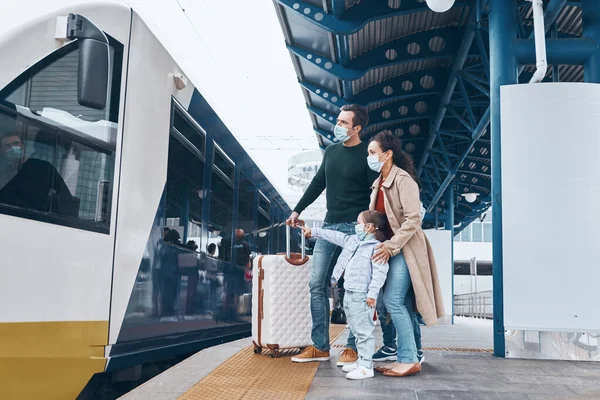 Plná délka rodiny se dvěma malými dětmi v ochranných obličejových maskách a stojící na nástupišti železniční stanice — Stock fotografie