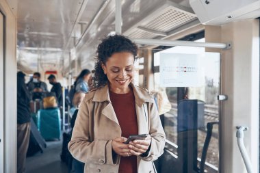 Akıllı telefon kullanan ve trenle seyahat ederken gülümseyen güzel olgun bir kadın.