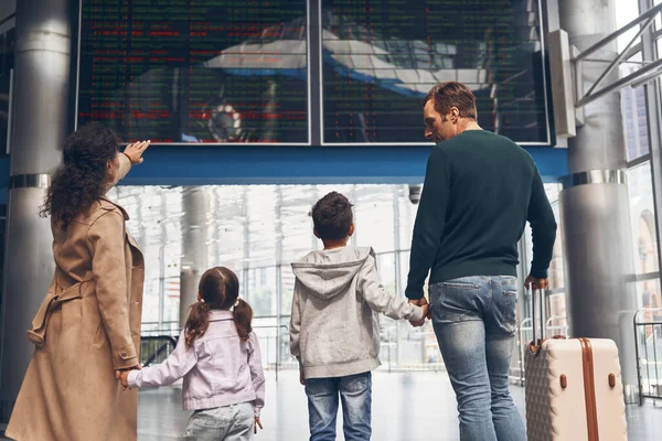 Bakifrån av familjen med två små barn tittar på flyginformationstavlan — Stockfoto