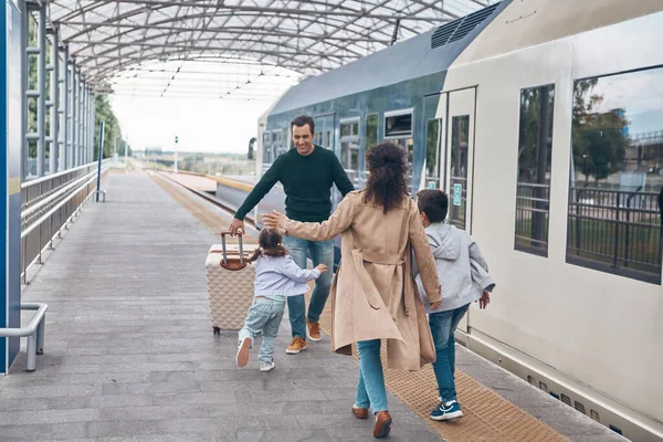Pleine longueur de femme heureuse et deux petits enfants rencontrant père sur la plate-forme de la gare — Photo