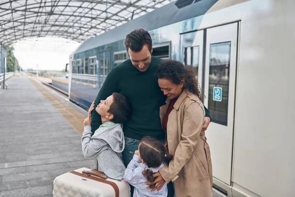 Famille heureuse avec deux petits enfants collant tout en se tenant sur la plate-forme de la gare ensemble — Photo