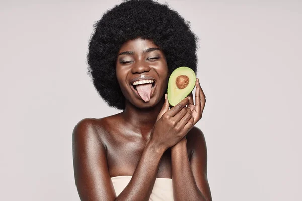 Portré gyönyörű fiatal afrikai nő gazdaság avokádó és grimaszolás — Stock Fotó