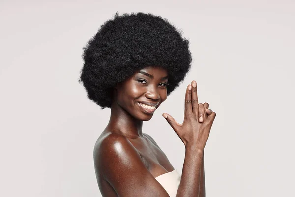 Retrato de una hermosa joven africana mirando a la cámara y haciendo gestos mientras está de pie sobre un fondo gris — Foto de Stock