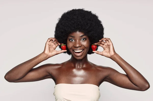 Portré gyönyörű fiatal afrikai nő kezében eper, mint fülbevaló és mosolygós — Stock Fotó