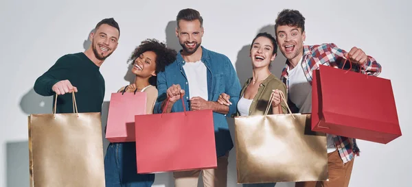 Group of young beautiful people in casual clothing carrying shopping bags and smiling — Stock Photo, Image
