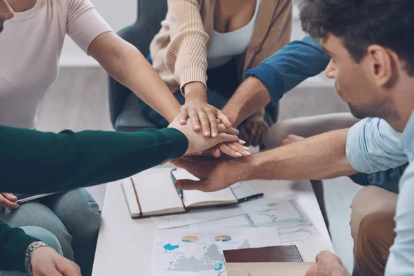 Nahaufnahme von oben, wie ein modernes Business-Team die Hände zusammenhält, während es gemeinsam im Büro sitzt — Stockfoto