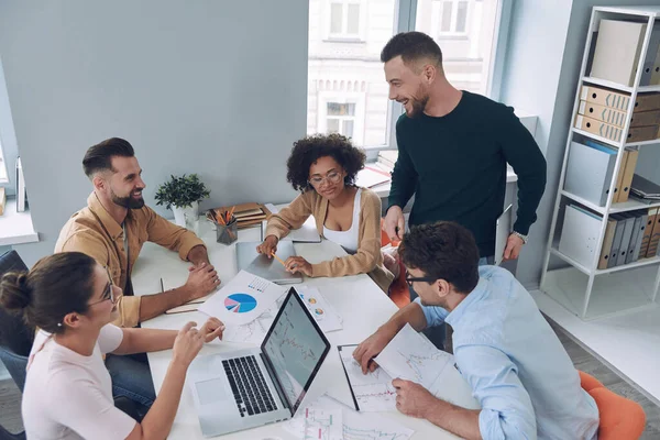Група впевнених молодих людей у розумному повсякденному одязі обговорює бізнес під час зустрічі в офісі — стокове фото